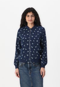 Tumesinine pommitusjacket, millel on lilleline muster, pehme kangas, lukuga sulgemine, ribikätked ja fiteeritud vöökoht.