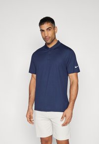 Sötétkék pólóing sima anyagból, klasszikus gallérral, három gombos kivágással és egy fehér Nike logóval a bal ujján.