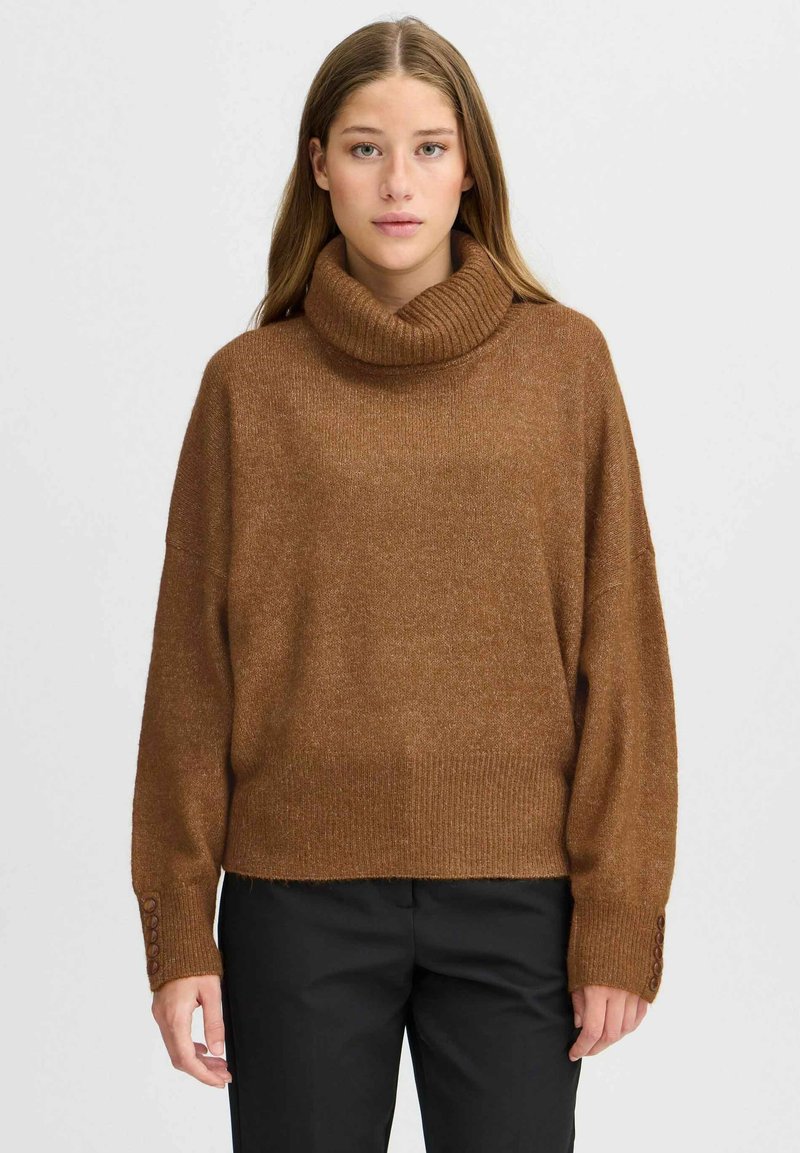 Pull en tricot marron avec un col roulé haut à côtes, coupe décontractée et accents de boutons sur les manches. Texture douce avec un design légèrement oversized.