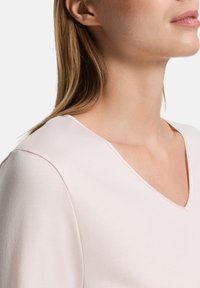 Top rosa claro con escote en V y textura suave. Detalles de costuras a lo largo del escote y el hombro añaden acentos sutiles.