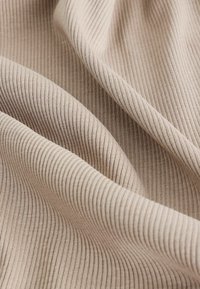 Beige ribbet stof med fine, vertikale linjer, der fremviser en blød tekstur og fleksibel fald. Materialet virker glat og letvægtigt.