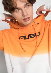 Orange- og hvid gradient hættetrøje med FUBU-logo i sort, snøre og frontlomme. Fremstillet i bomuldsstof, med casual pasform og blød tekstur.