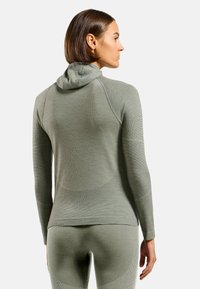 Haut long à manches, de couleur vert clair, texturé avec une capuche, présentant un matériau côtelé et un design ajusté. Détails de couture le long du dos et des manches.