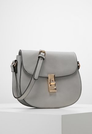 Jasnoszara skórzana torba na siodło z regulowanym paskiem i prostokątnym zatrzaskiem w złotym odcieniu, na białej powierzchni.