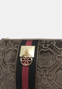 Borsa di stoffa marrone con motivo geometrico in rilievo, dotata di una chiusura dorata, una striscia nera e rossa e un accento con logo circolare.
