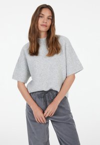 Light grey, ribbed knit sweater with short sleeves and a high neckline, paired with grey drawstring trousers. Simple design, soft texture.