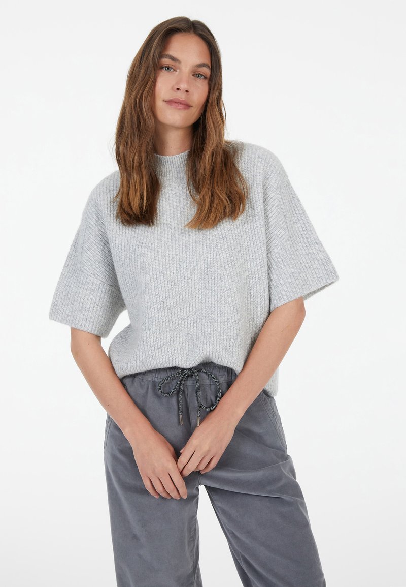 Light grey, ribbed knit sweater with short sleeves and a high neckline, paired with grey drawstring trousers. Simple design, soft texture.