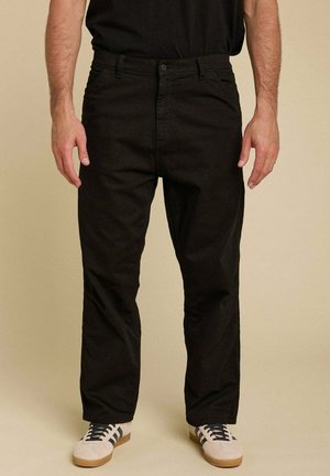 Pantalons en coton noirs avec une coupe droite, dotés d'une fermeture éclair et de cinq poches. Associés à des baskets beiges et à un t-shirt noir.