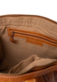 Intérieur en cuir marron d'un sac avec une poche zippée, un tissu brun contrastant et des accents cousus. Comprend un détail de label.