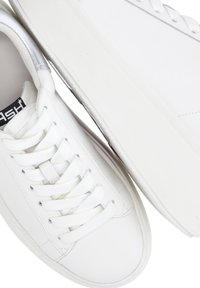 Sneakers bianchi in pelle con lacci piatti, punta rotonda e suola testurizzata. Presentano un'accento argentato sul tallone e un marchio sulla linguetta.