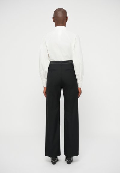 Valge pika varrukaga särk, millel on volangvarrukad, koos kõrge taljega mustade laiade pükstega. Sile kangas, minimalistik disain, nähtavad mustrid puuduvad.