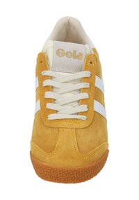 Gulfärgad mockaskosportskor med vita ränder, krämfärgade snören och texturerad gummisula. Har en vadderad tunga märkt "Gola."
