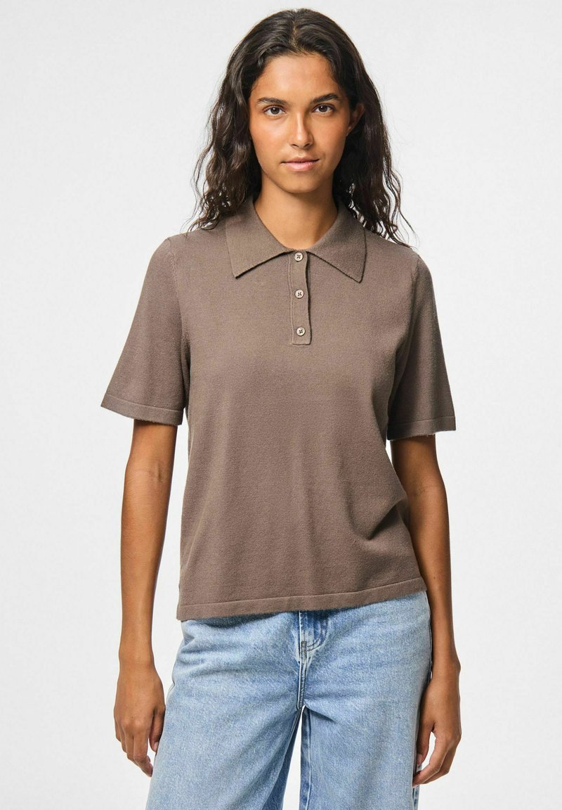 Brun kortärmad polo med platt krage och knäppning med tre knappar, tillverkad av strukturerad tyg, ihop med ljusblå jeans.