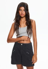 Canotta grigia e pantaloni cargo neri con tasche laterali, chiusura a bottone e dettagli metallici. Tessuto liscio, vestibilità rilassata, design casual.