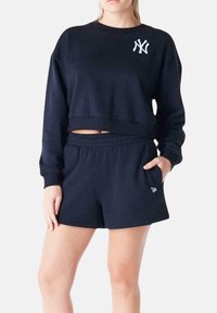 Felpa cropped blu navy con logo bianco sul petto, abbinata a pantaloni shorts blu navy coordinati, dotati di vita elastica e tasche laterali.