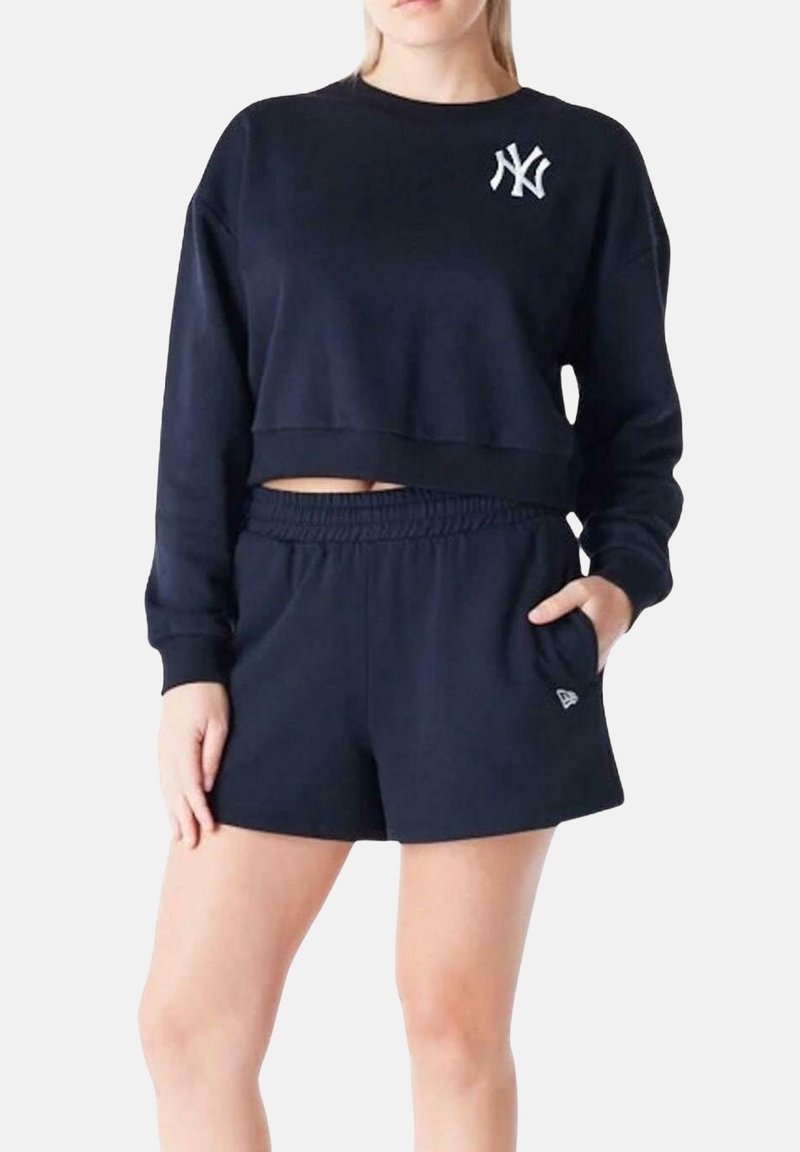 Felpa cropped blu navy con logo bianco sul petto, abbinata a pantaloni shorts blu navy coordinati, dotati di vita elastica e tasche laterali.