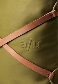 Borsa verde oliva realizzata in materiale testurizzato, chiusa con una tracolla diagonale in pelle marrone con cuciture e logo impresso.