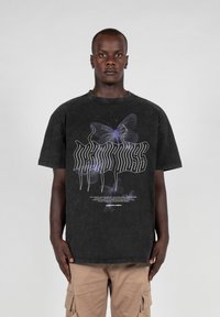 Sort bomulds t-shirt med et grafisk design af lilla sommerfugle og stiliseret tekst på fronten. Korte ærmer, afslappet pasform.