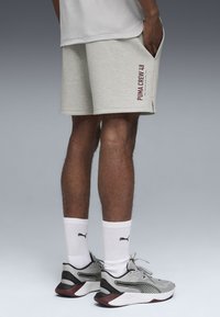 Graue Shorts mit Seitentaschen und maroonem "PUMA CREW 48"-Text. Weiße Sportsocken kombiniert mit grauen und roten Turnschuhen.