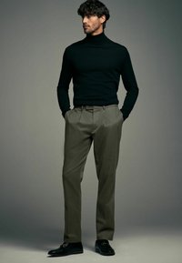 Pull-over noir à col roulé, pantalon beige à plis et mocassins noirs avec accents dorés. Textures lisses, design ajusté et palette de couleurs neutres.