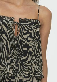 Robe sans manches noire et beige avec un motif zèbre, texture plissée, décolleté froncé et un détail de nœud à l'avant.