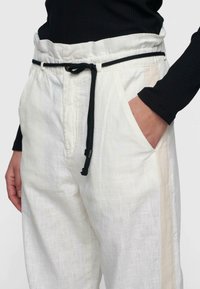Lichte witte broek met een gestructureerde afwerking, een zwarte trekkoord, zijzakken en een beige streep langs de zijkant.