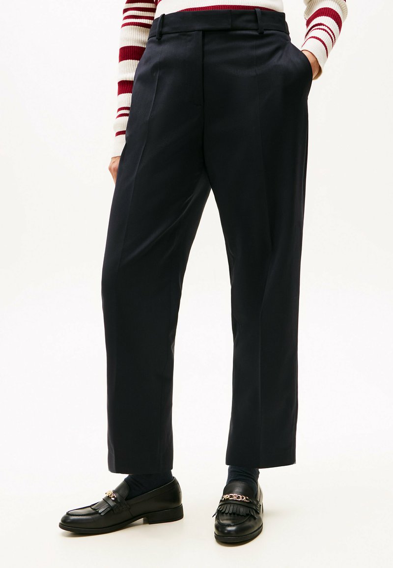 Pantaloni blu scuro con vestibilità sartoriale, caratterizzati da una vita alta e pieghe. Tessuto liscio, tasche laterali e orlo corto pulito.