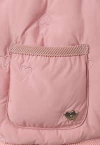 Tissu matelassé rose avec une poche en forme de cœur dotée de bordure en velours côtelé et de broderie en forme de cœur. Petit accent en matériel en forme de cœur sur la poche.