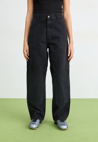 Sorte denim vide benbukser med store lommer, høy midje og en ren finish. Kombinert med grå treningssko.