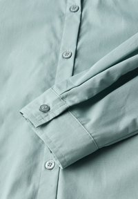 Camicia azzurro chiaro a maniche lunghe con polsini abbottonati e patta frontale con bottoni rotondi.