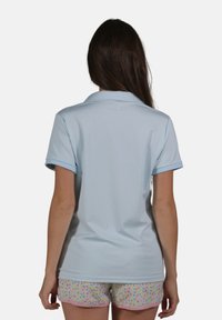 Polo bleu clair avec col, manches courtes et poignets contrastants bleu clair. Texture lisse. Associé à un short à motif floral.