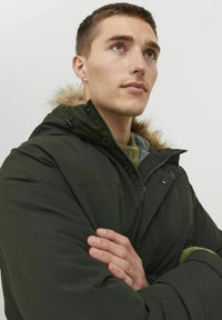 Dark green puffer jacket with a fur-lined hood, zip and snap closures, and textured knit detail visible at the collar.