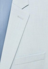 Jasnoniebieska marynarka wykonana z teksturowanej tkaniny. Posiada wykładany kołnierz, pojedynczą kieszeń na piersi oraz subtelne detale przeszycia na kołnierzu.