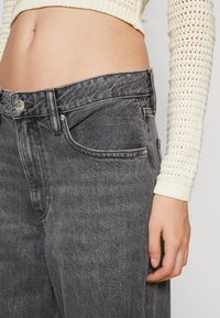 Grå denimjeans med hög midja, femficksdesign och subtila blekningar. Har en metallknapp och mässingsnitar för extra detalj.