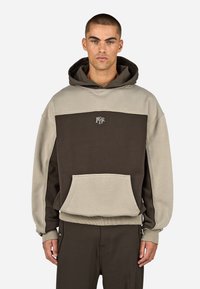 Hætte sweatshirt i brunt og beige bomuld, med en frontlomme, ribbede ærmer og et logo på brystet, designet i farveblokstil.