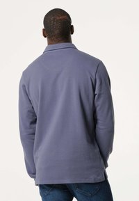 Lange mouwen pullover van zachte, donkere lavendelstof. Heeft een kraaghalslijn en zijsplitten voor gemak in beweging.