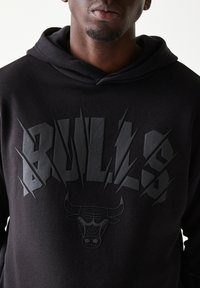 Μαύρο φούτερ με κουκούλα που διαθέτει έντονο, ανάγλυφο γράφημα "BULLS" και ένα σήμα ταύρου. Λείο, υφή υφάσματος με κουκούλα και κορδόνι.