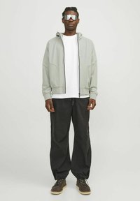 Light gray zip-up jacket with hood, white shirt underneath, black baggy pants, and brown boots. Reflective sunglasses complete the outfit.