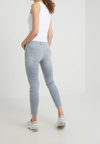 Jeans skinny azzurri chiari con una texture liscia, design a cinque tasche e dettagli di cucitura sottili, abbinati a un top senza maniche bianco e sneakers.