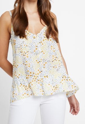 Top sans manches floral avec un col en V, présentant un fond blanc, des fleurs jaunes et bleues, et un ourlet volanté. Tissu léger.