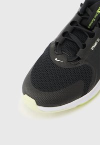 Μαύρο αθλητικό παπούτσι με επάνω μέρος από διαπνέον πλέγμα, υφασμένα επικάλυψη, φωτεινές πράσινες λεπτομέρειες και λευκή εξωτερική σόλα. Ρυθμιζόμενο κλείσιμο με κορδόνια.