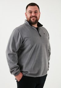 Grå fleecepullover med lynlås i kraven, tekstureret stof og en vandret søm over brystet; har et subtilt logo på forsiden.