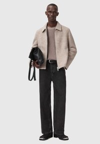 Beige uldblandingsjakke, lysegrå strikketrøje, sorte denim bukser og sort struktureret håndtaske, der har en glat overflade og lige pasform.