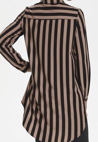 Blusa a maniche lunghe con strisce verticali nere e beige, realizzata in un tessuto morbido con orlo curvo e dettagli con polsini abbottonati.