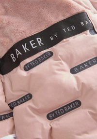 Indvendighed af rosa pufferjakke med blød faux pels og et sort stofmærke med teksten "BAKER by TED BAKER" i hvid tekst mod en glat baggrund.