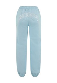 Svetlomodré tepláky s elastickým pásom. Obsahujú metalické strieborné texty a malé ozdoby na chrbte. S manžetami na členkoch.