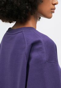 Purple sweatshirt featuring a crew neckline, textured fabric, and a relaxed fit, with visible stitching and a clean design.