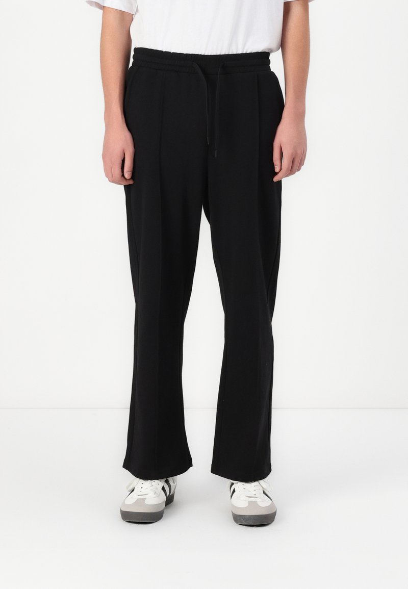 Black, loose-fitting pants with an elastic waistband and drawstring. Made of soft fabric, featuring front pleats and wide legs.