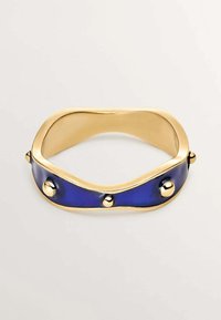 Pulsera de puño de oro con diseño ondulado; presenta una banda de esmalte azul y tres acentos esféricos de oro en la superficie. Textura suave.