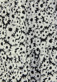 Svart och vit blommig tyg med små prästkragar och en texturerad mönster, sydd med veck som skapar ett lagerutseende.